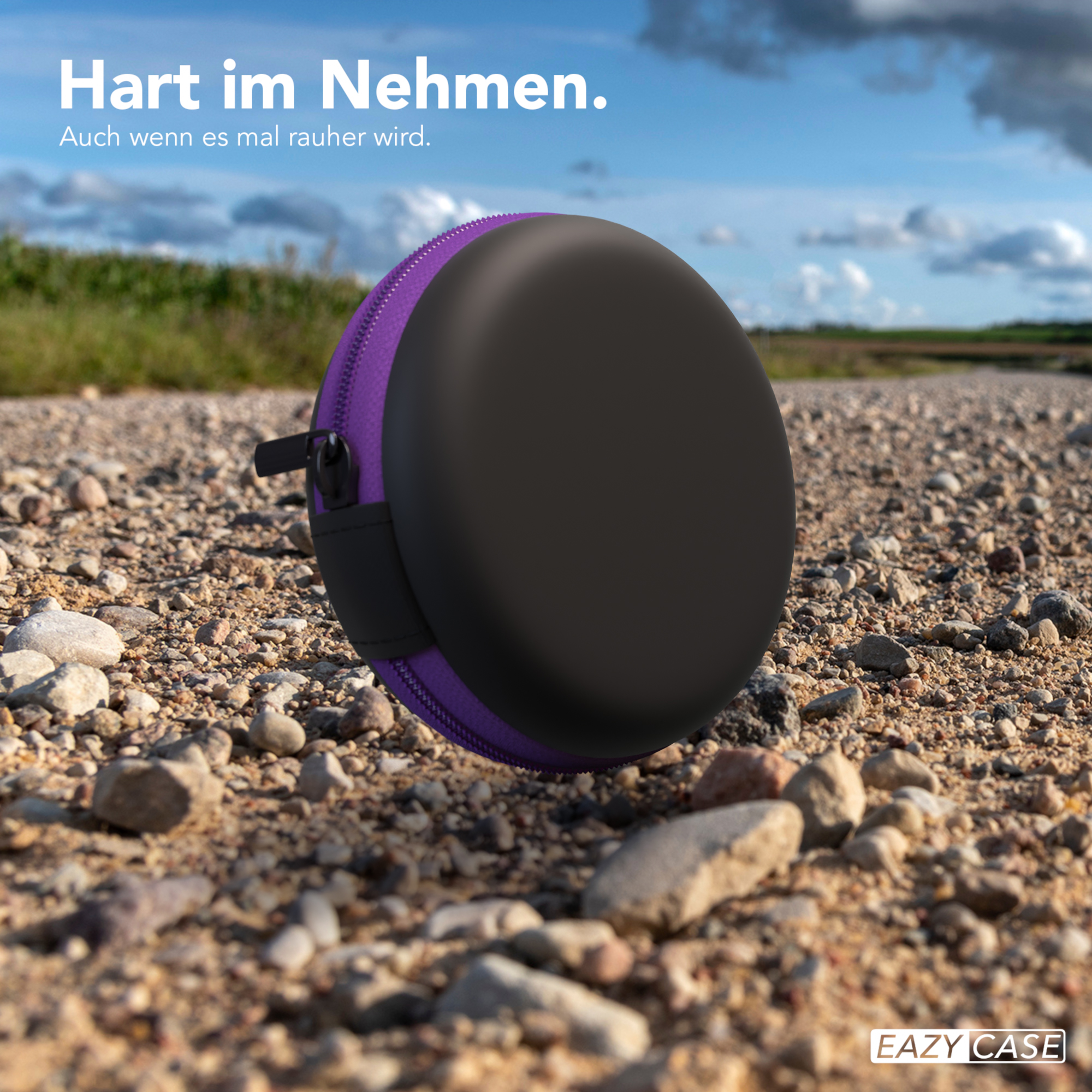 Ein schwarzes und lilafarbenes kreisförmiges Etui auf einem Schotterweg, mit Text: 'Hart im Nehmen'.