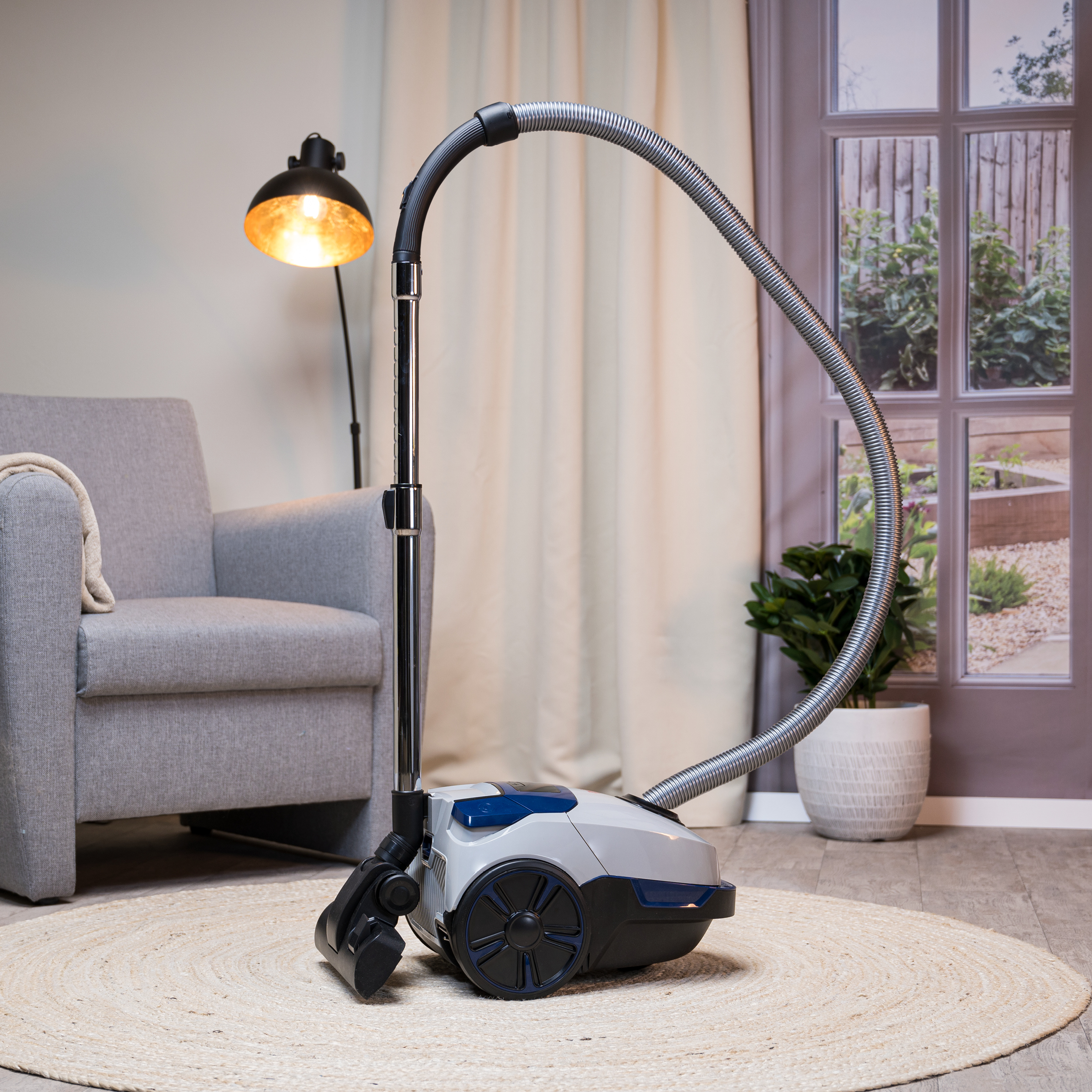 Stofzuiger op een kleed met een lamp en een raam op de achtergrond.