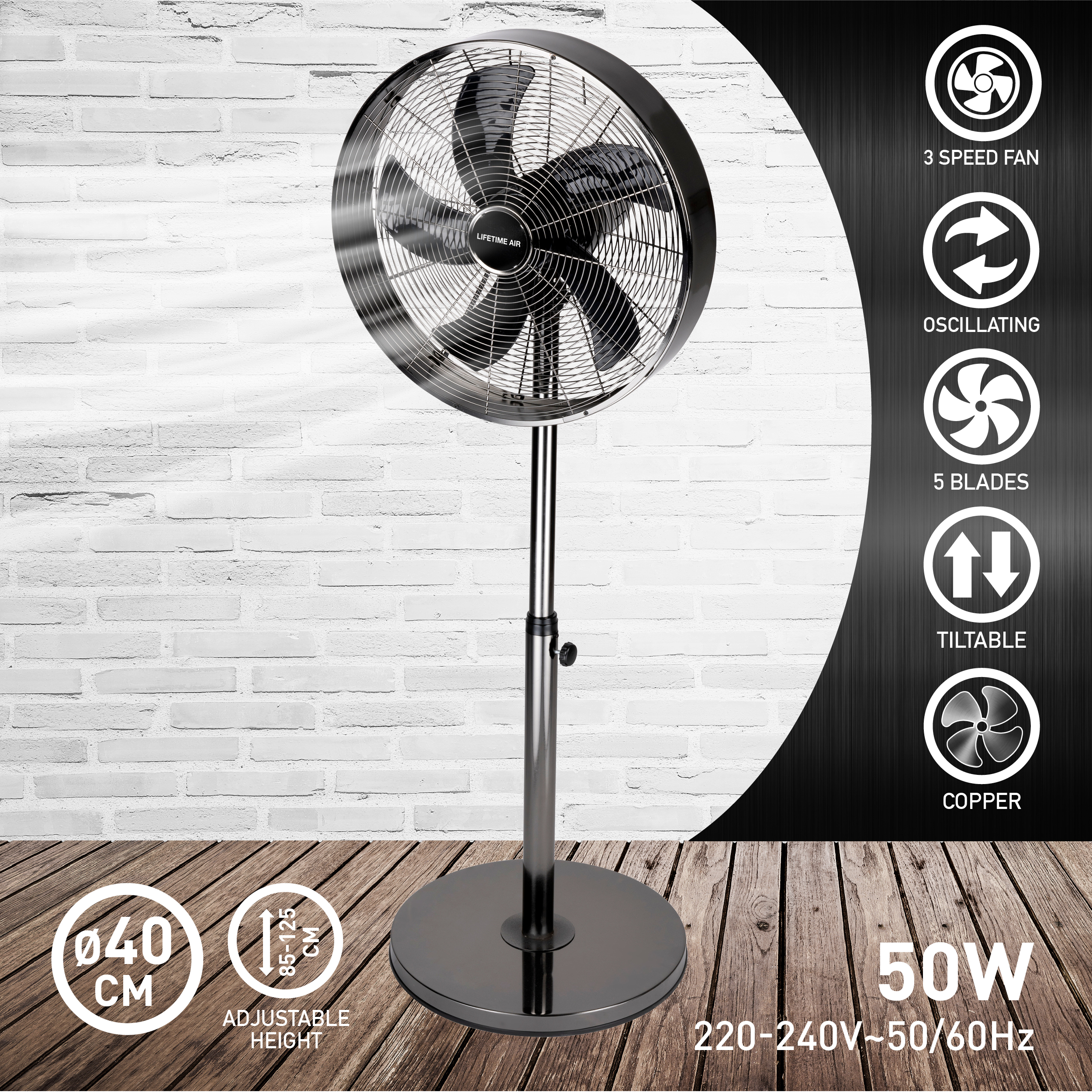 Black fan on a stand with 5 blades. It is on a wooden floor in front of a brick wall.