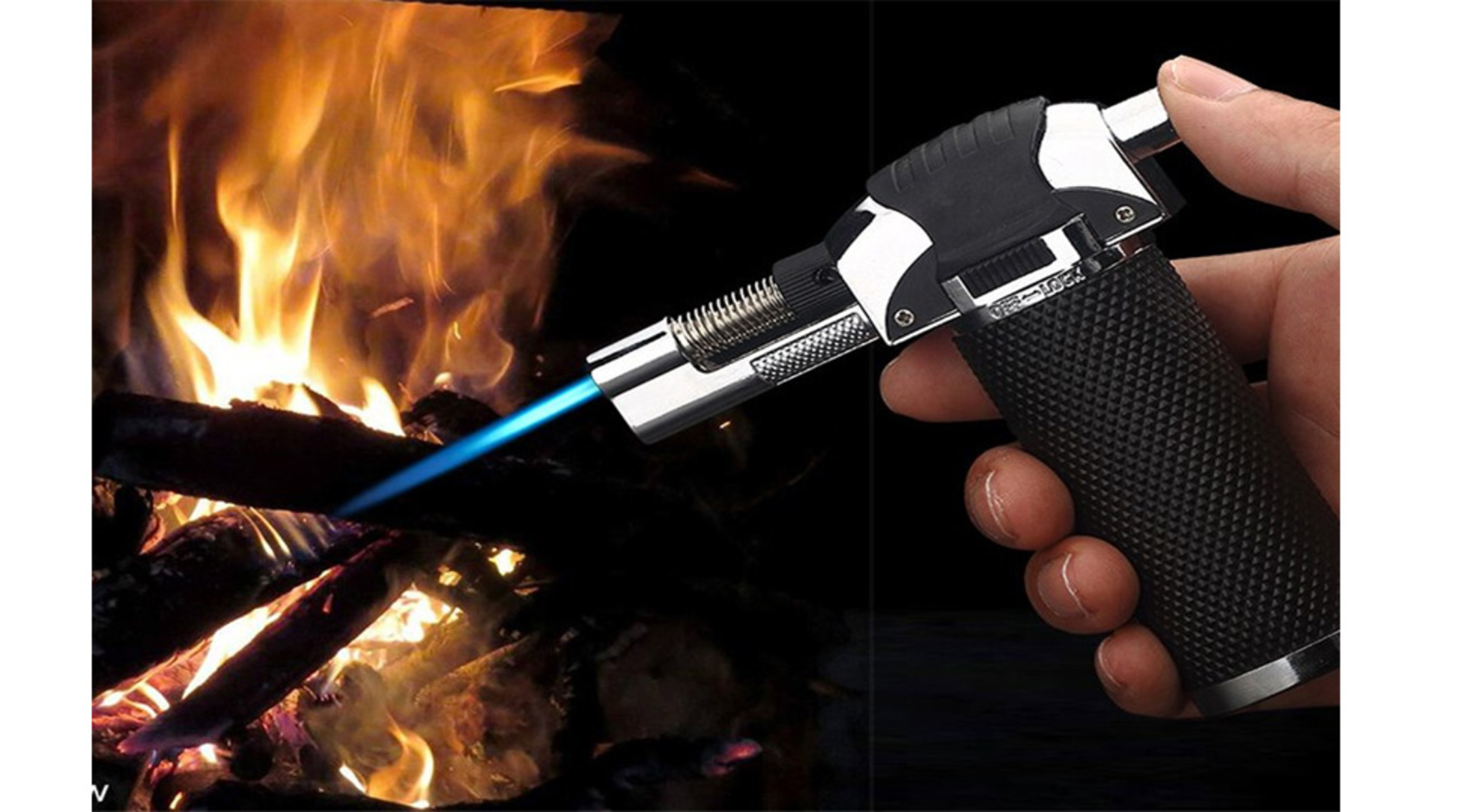 Eine Hand, die ein silbernes und schwarzes Fackel-Feuerzeug hält, mit einer blauen Flamme vor einem Feuer.