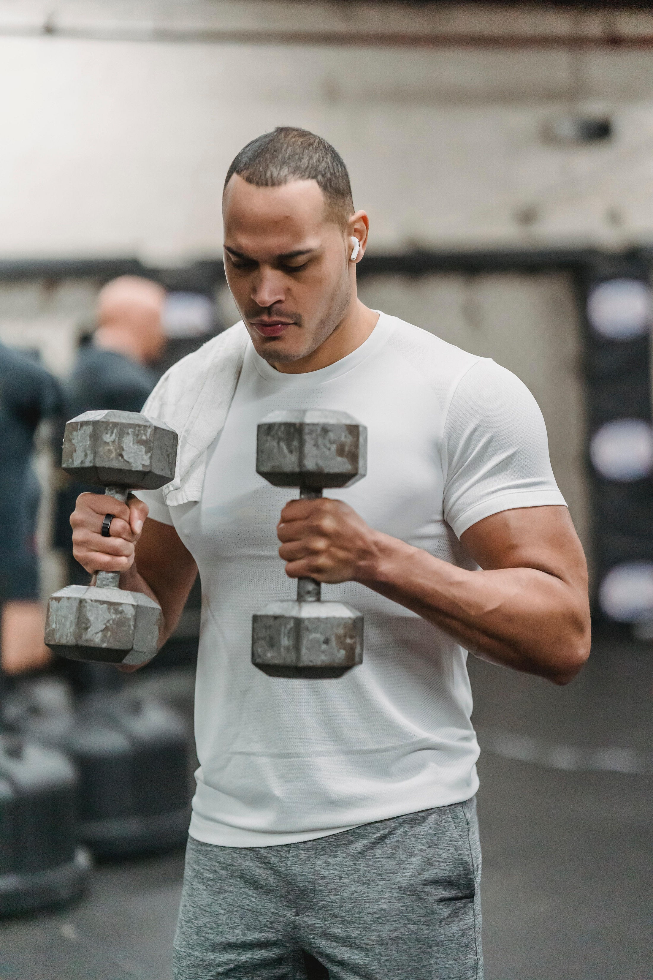 Mann im Fitnessstudio, der Kurzhanteln hält und Ohrhörer trägt.