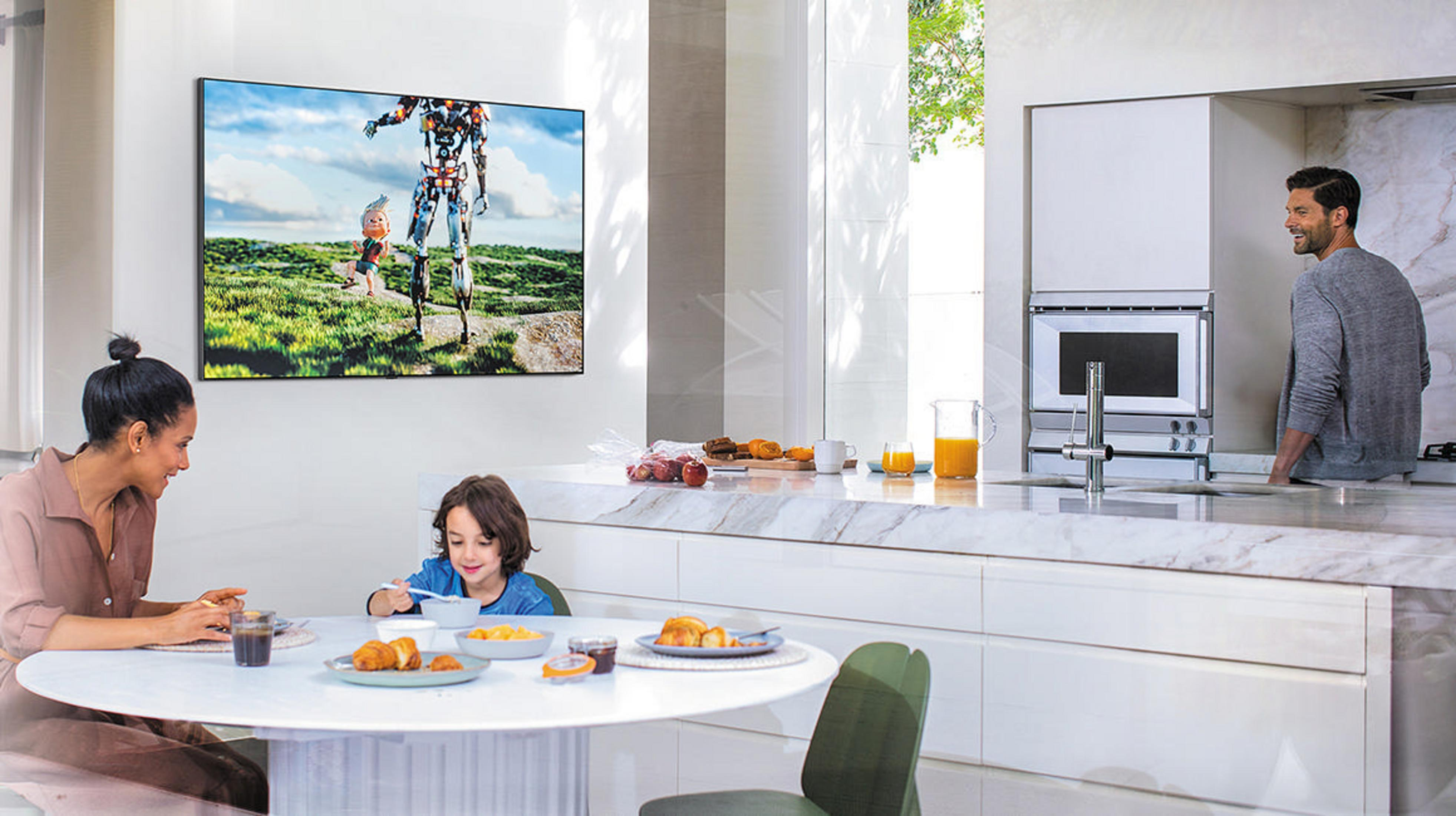 Rodzina przy stole ogląda telewizję. Telewizor pokazuje robota i dziecko, biała kuchnia, nowoczesny design.