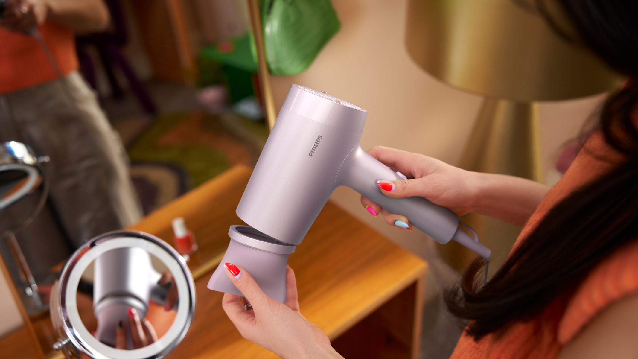 Kobieta trzymająca różową suszarkę do włosów, z lustrem i innymi przedmiotami.