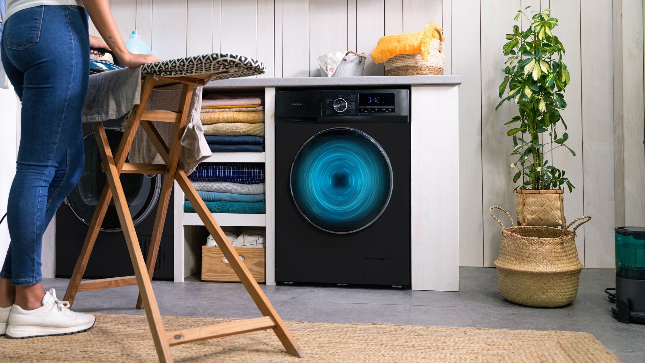 Kobieta prasująca ubrania w pralni, z pralką i suszarką.