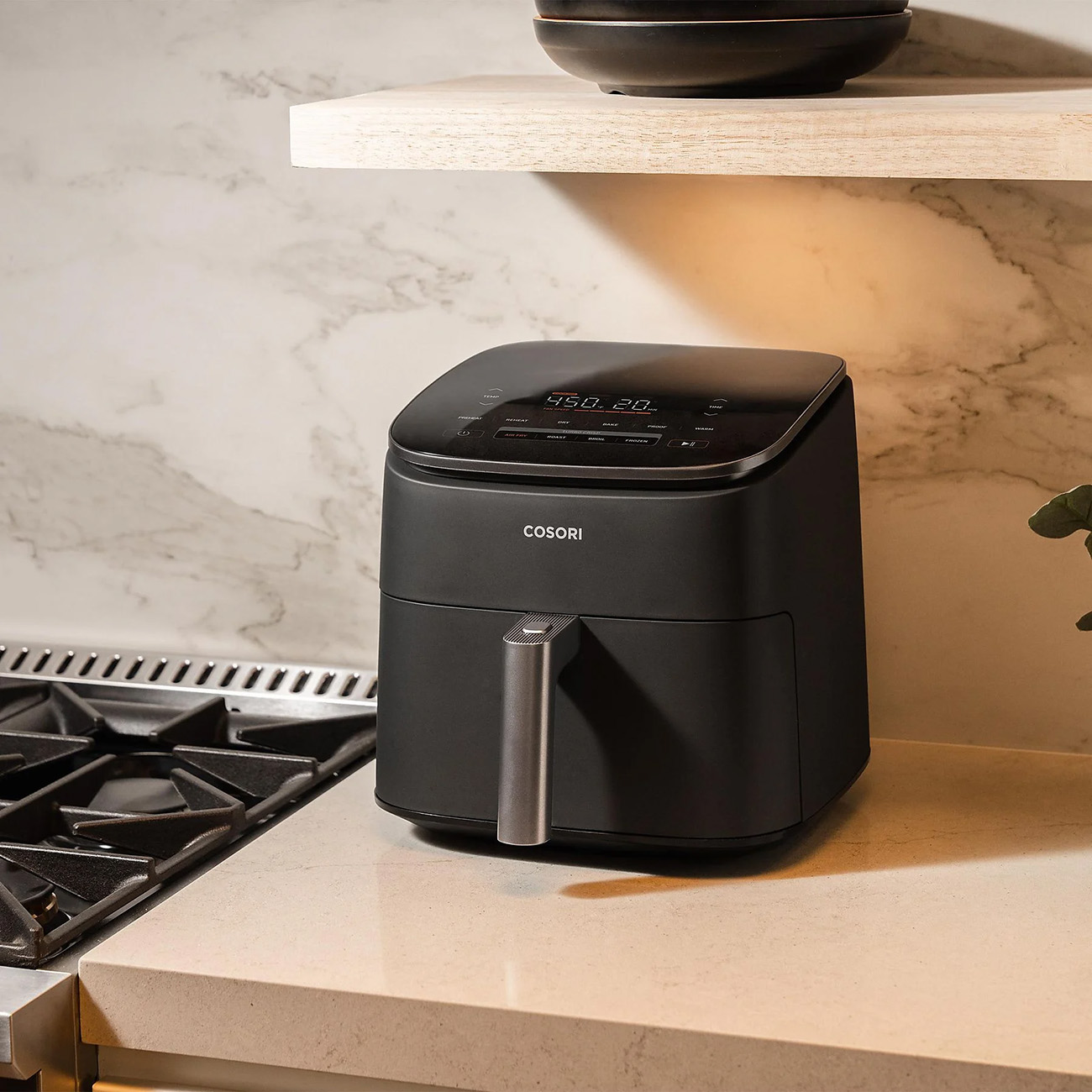 Czarna frytkownica Cosori na blacie, marmurowa ściana.