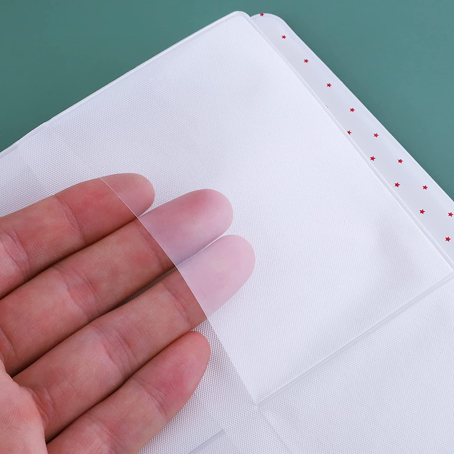 Hand, die ein transparentes Kunststoffblatt über einem weißen Notizbuch hält.