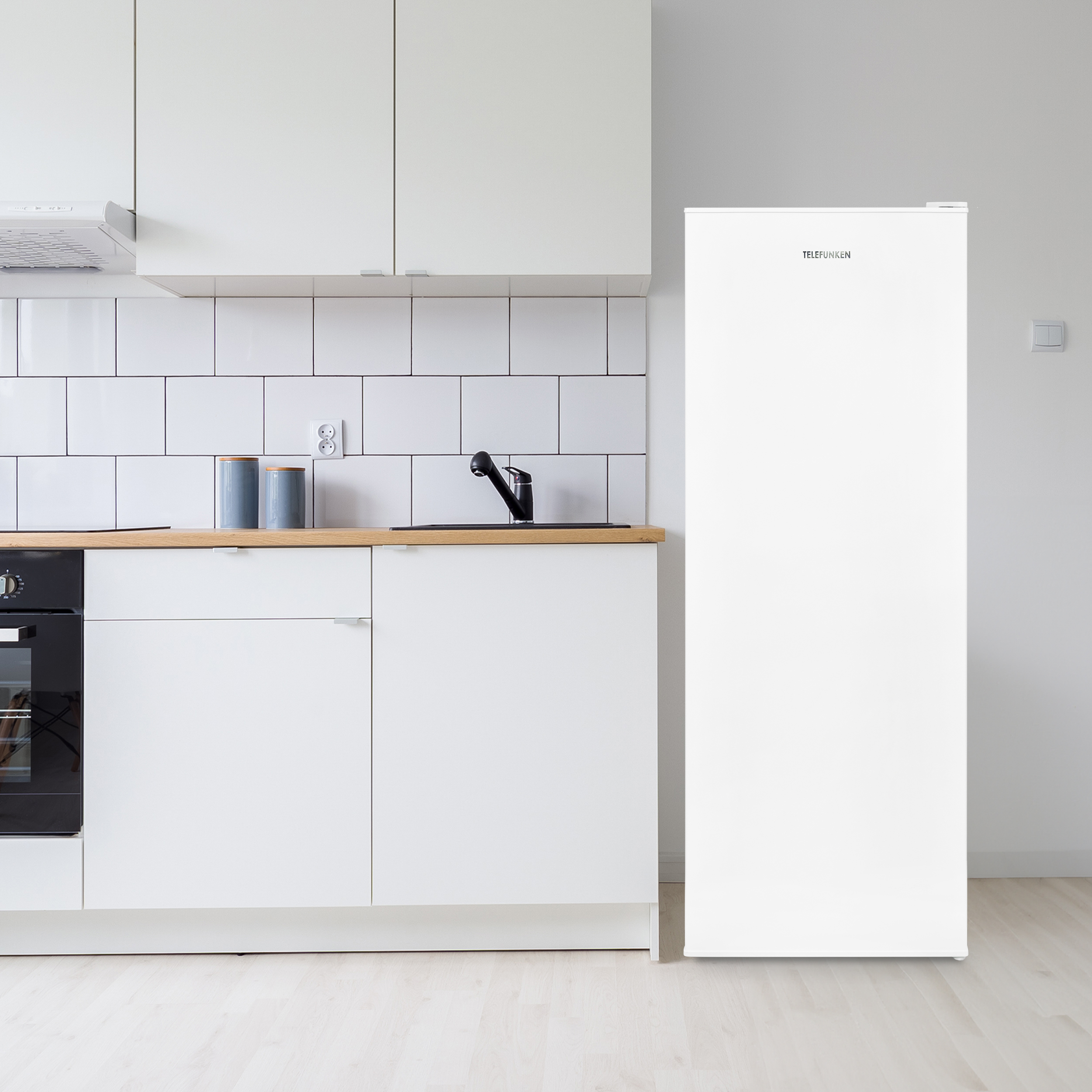 Weißer Kühlschrank in einer weißen Küche mit Holz-Arbeitsplatte und schwarzen Geräten.