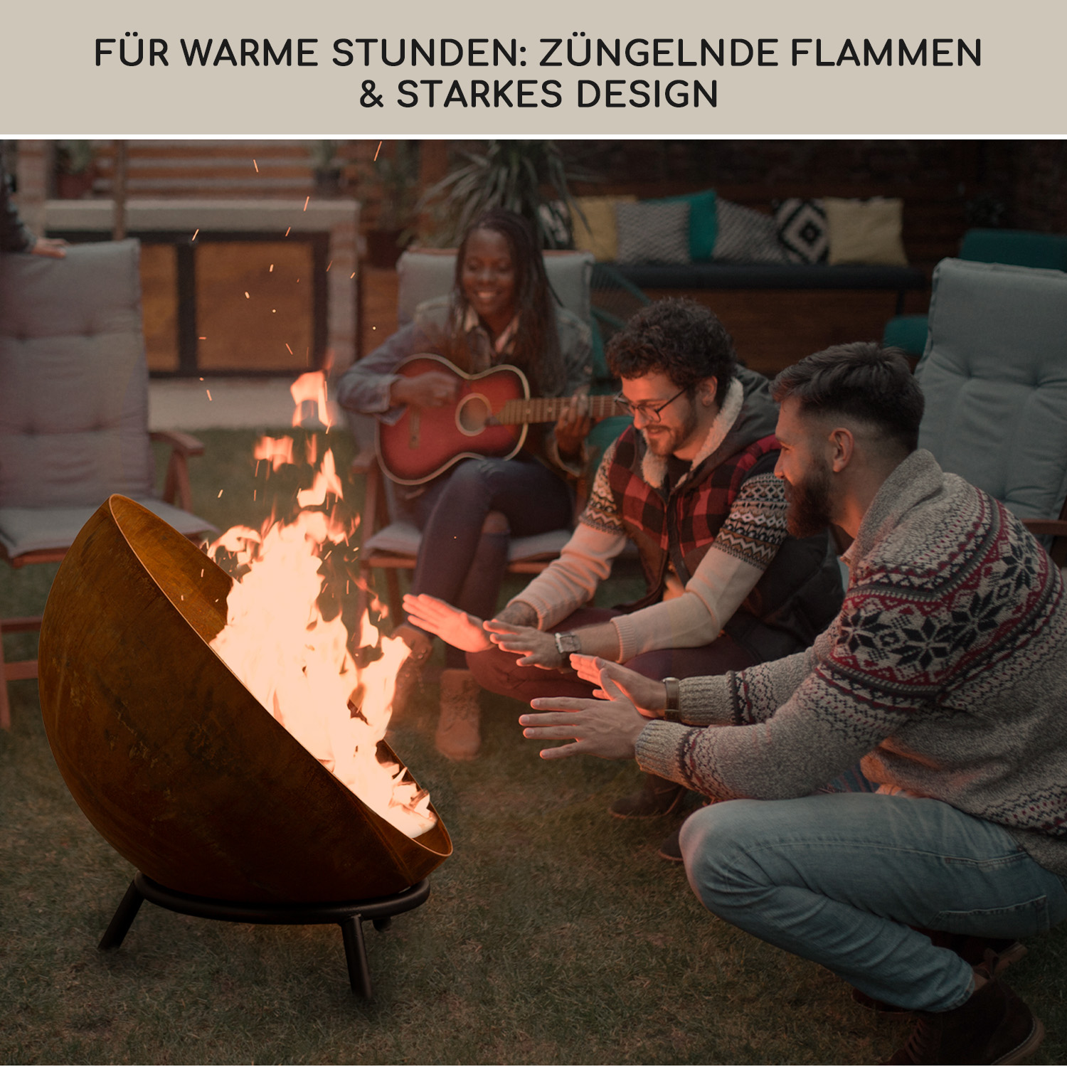 Leute um eine Feuerstelle, mit Flammen und Funken sichtbar. Eine Person spielt Gitarre.