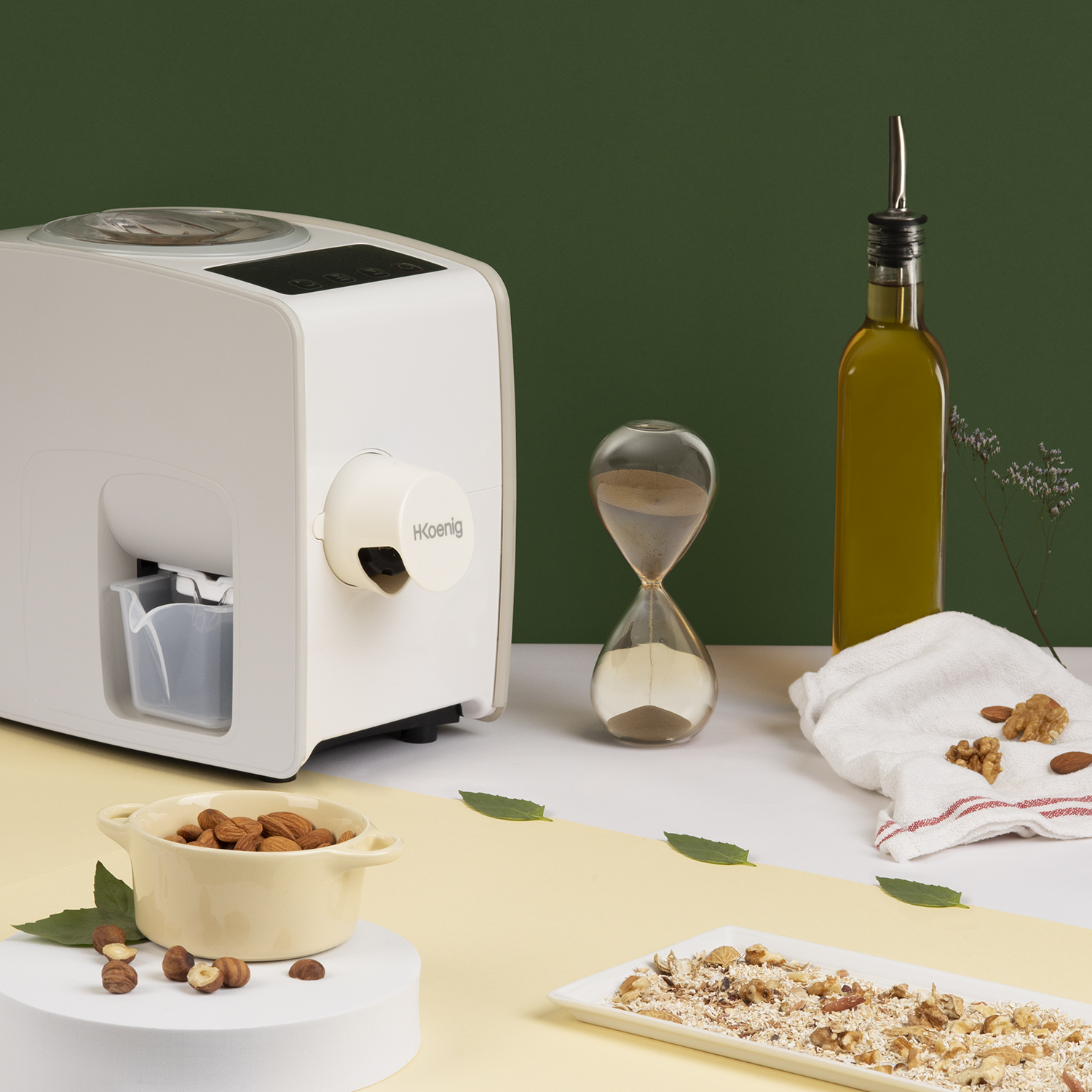 Una pressa per olio, clessidra, bottiglia d'olio, mandorle e noci su superficie bianca.