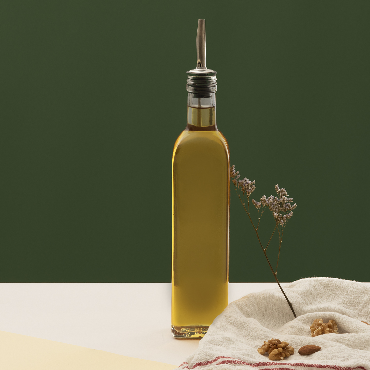 Bottiglia di olio d'oliva con beccuccio, noci e rametto su superficie bianca, sfondo verde.