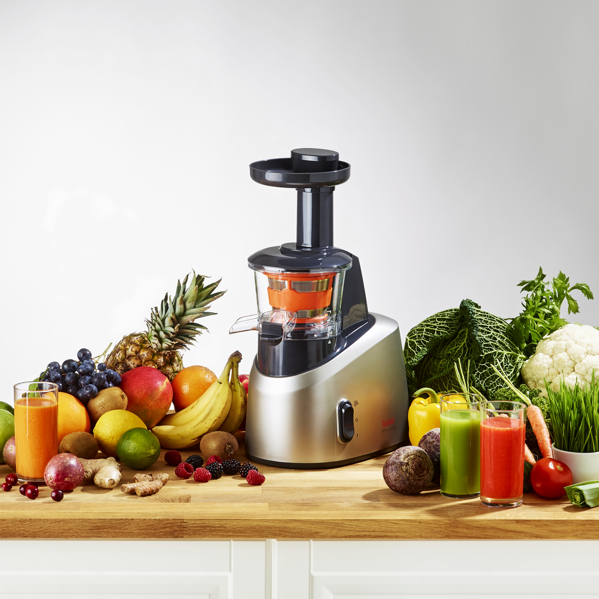 Una exprimidora con varias frutas y vasos de jugo. Piña, plátano y otras frutas son visibles.