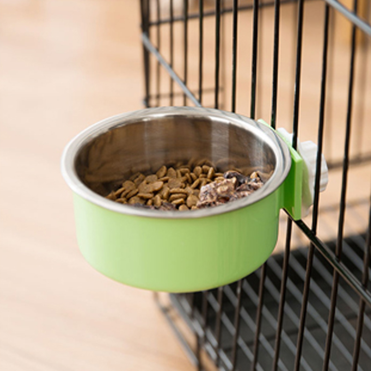 Eine grüne Schüssel mit Tierfutter, befestigt an einem schwarzen Käfig. Die Schüssel ist aus Metall.
