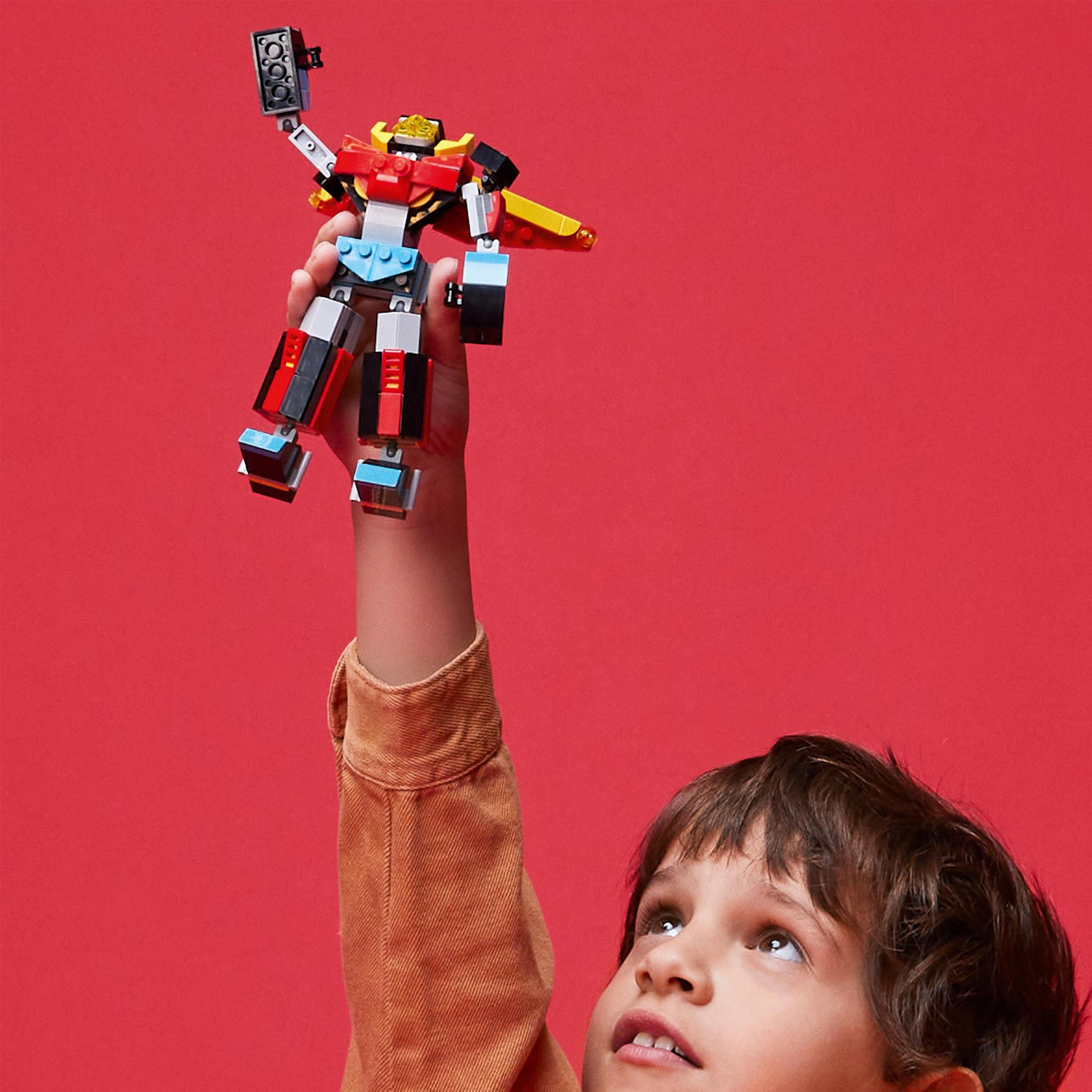Un niño sostiene un juguete robot Lego sobre fondo rojo.
