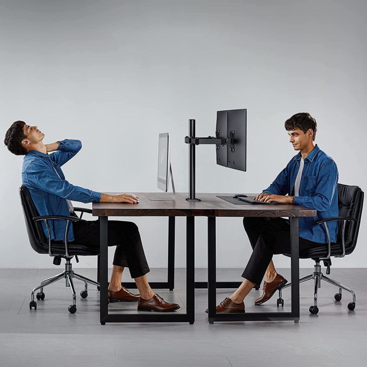 Zwei Männer sitzen an einem Tisch mit einem Monitor. Einer schaut hoch, der andere tippt.
