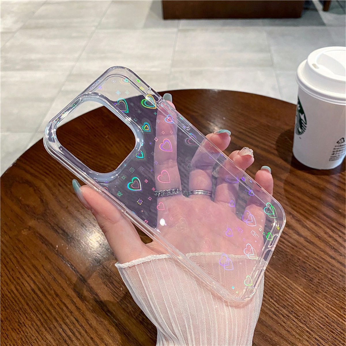 Hand hält eine durchsichtige Handyhülle mit Herzen und Starbucks-Becher.