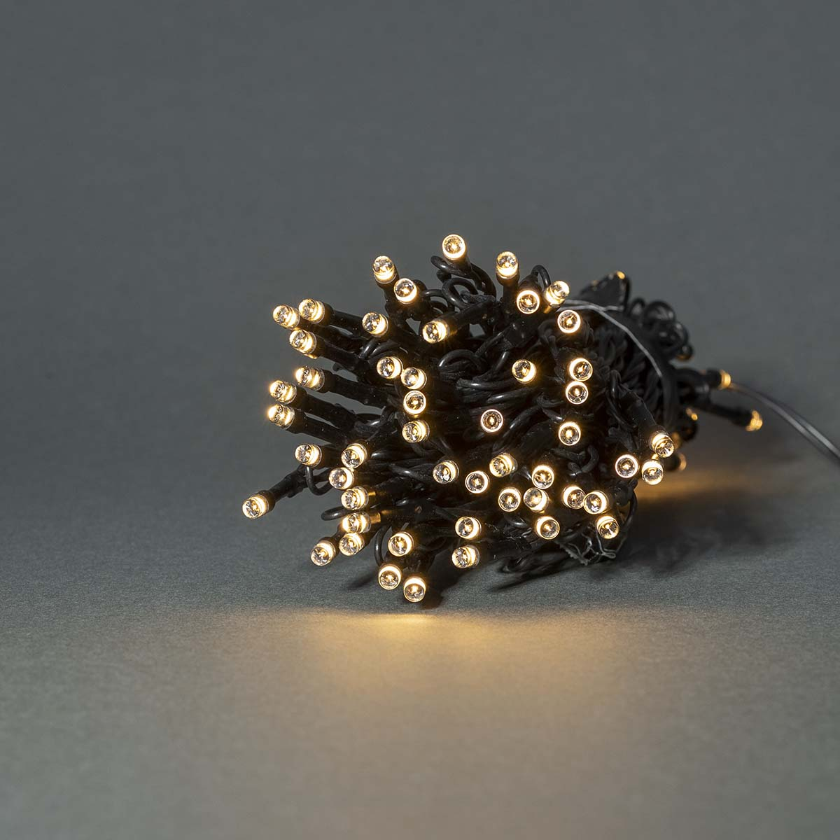 Fascio di luci a stringa nere con molte piccole lampadine illuminate su una superficie grigia.