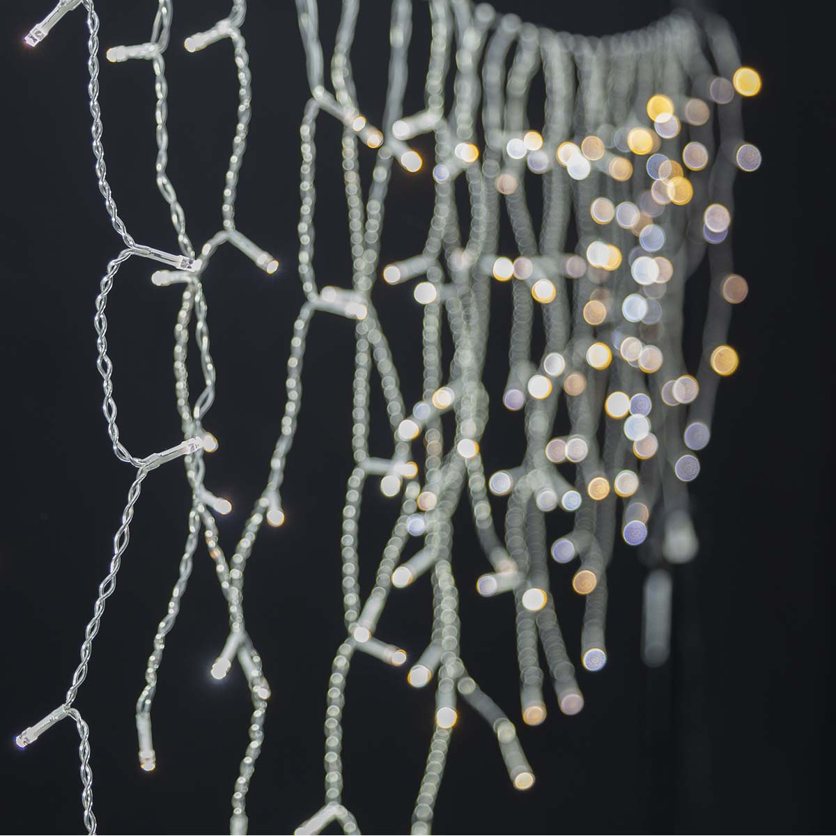 Zbliżenie na wiele pasm białych lampek choinkowych z czarnym tłem, tworzące bokeh.