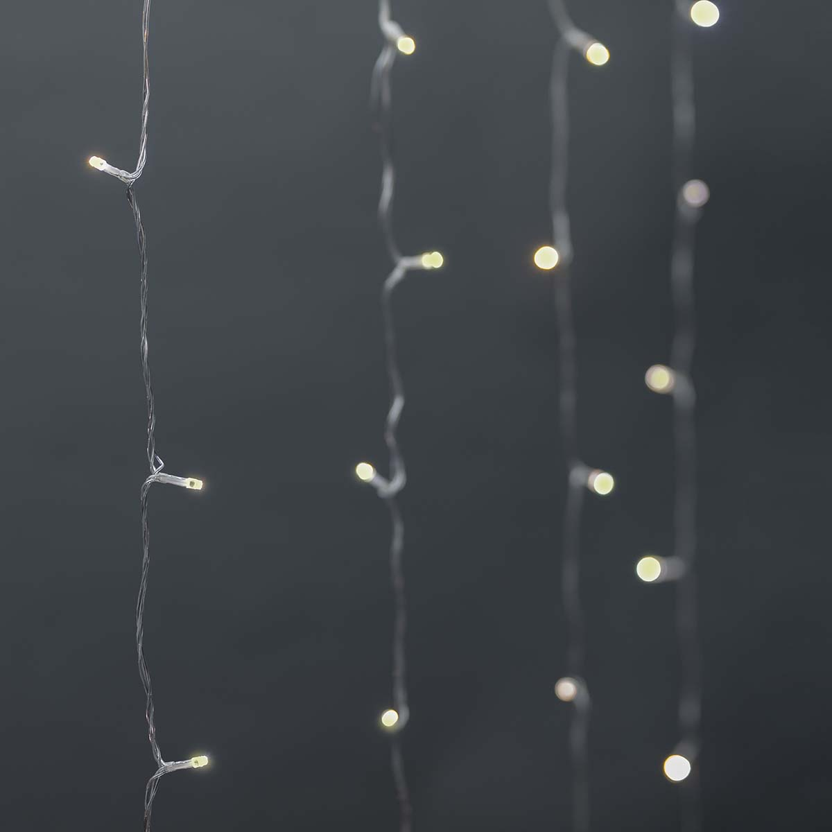 Kilka sznurów białych świateł wiszących na szarym tle. Światła są równomiernie rozmieszczone.