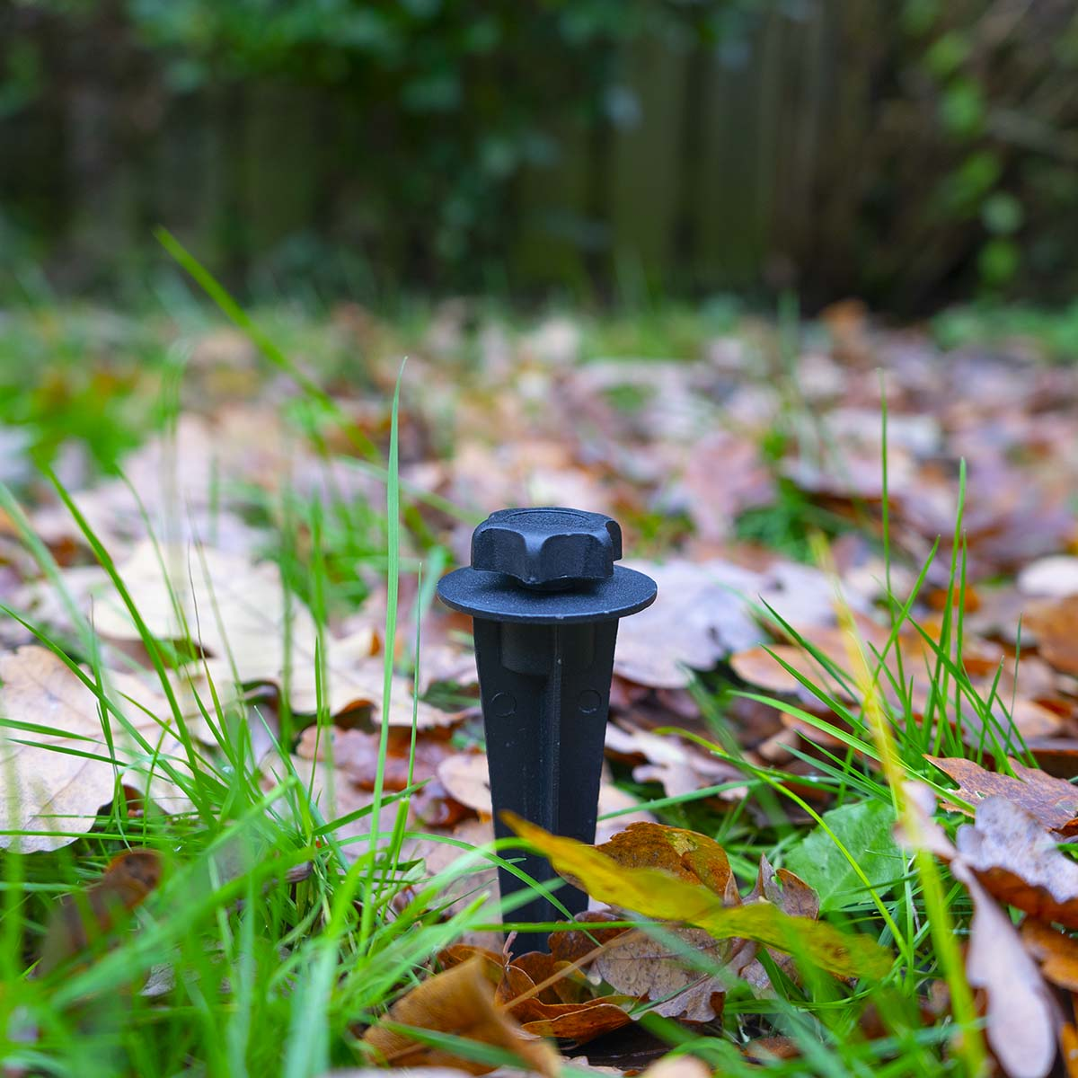Zwarte paal in gras en gevallen bladeren. De paal heeft een zwarte dop en een puntig uiteinde.