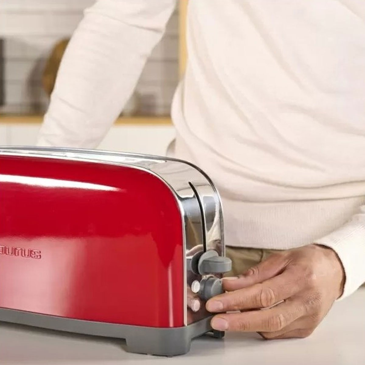 Una tostadora roja con una persona ajustando la configuración. Escena de cocina.