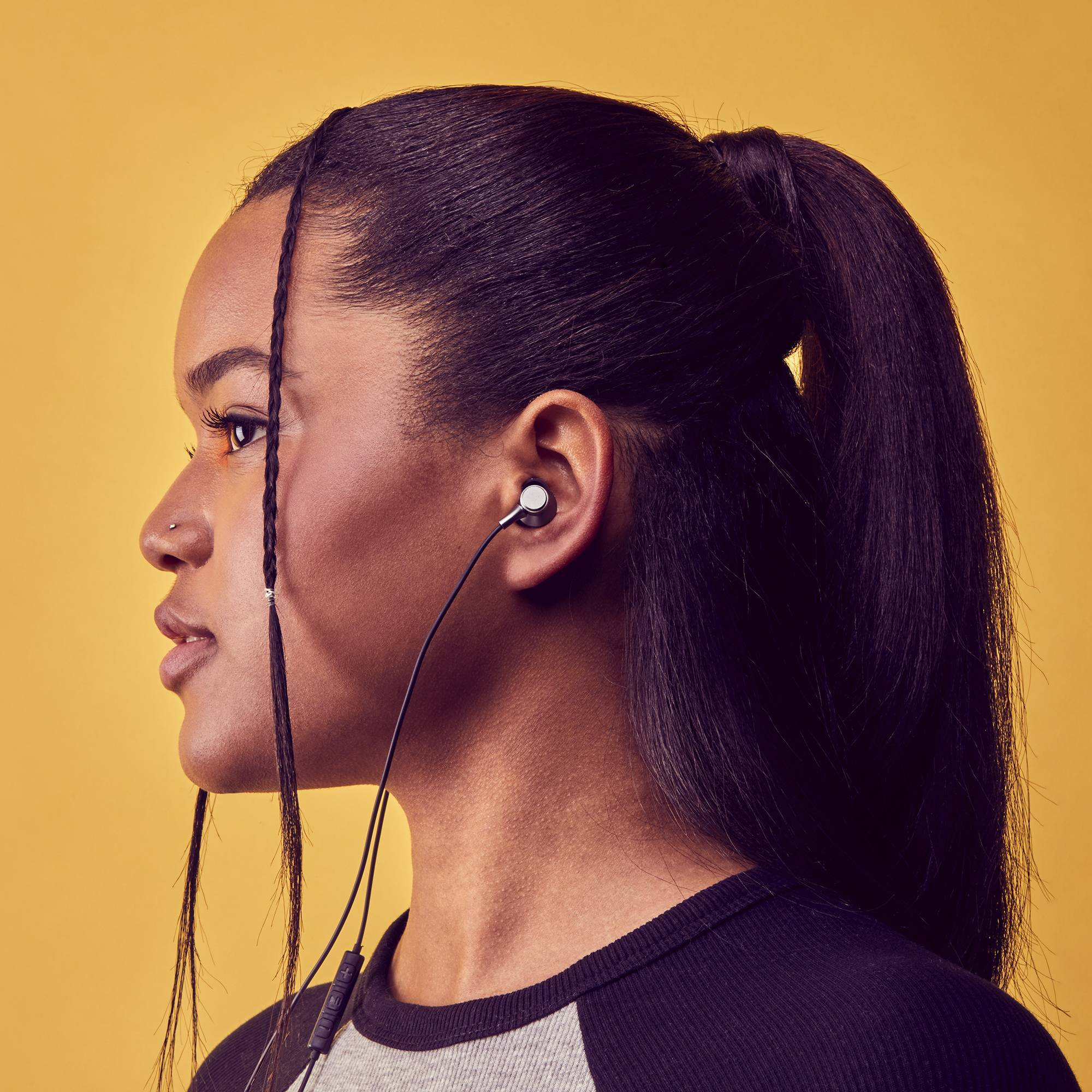 Una mujer con un auricular en la oreja, coleta, sobre fondo amarillo.