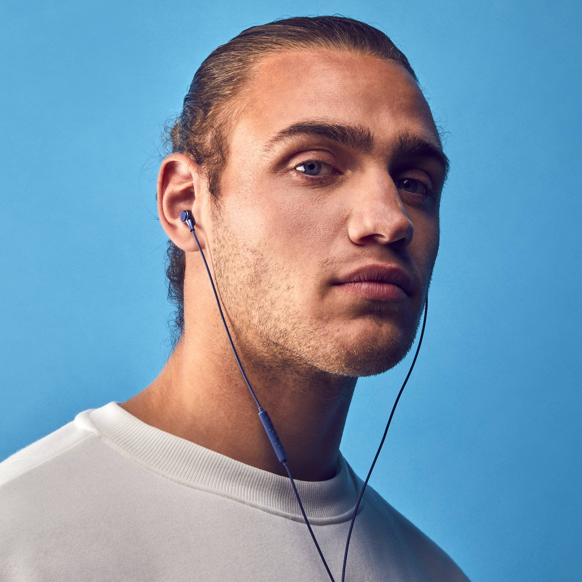 Un uomo con auricolari, sfondo blu. Guarda la fotocamera.