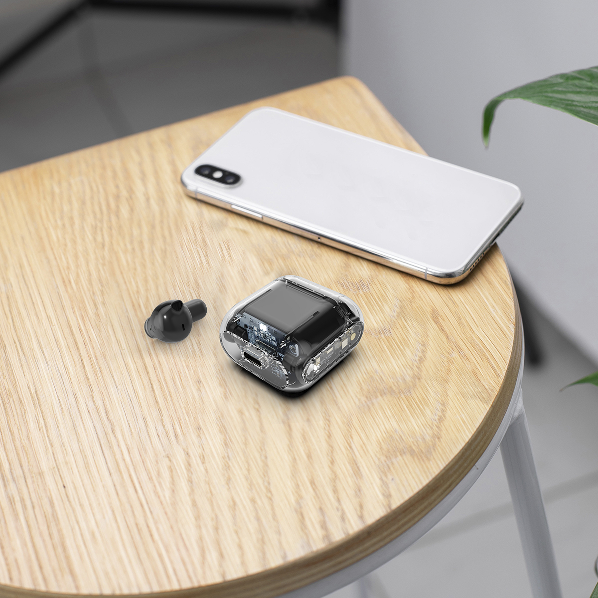 Ein kleiner kabelloser Ohrhörer und sein Ladeetui liegen auf einem Holztisch neben einem Smartphone.