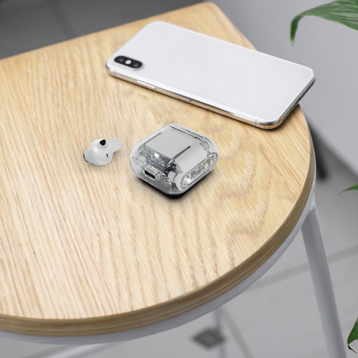 Ein weißes Telefon und eine Ladehülle mit einem Ohrhörer auf einem Holztisch, Hintergrund eine Pflanze.
