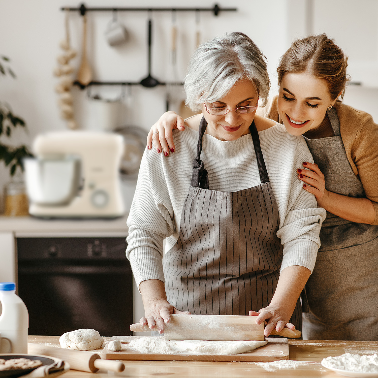 Una donna e una donna anziana stendono l'impasto insieme in cucina, sorridendo.