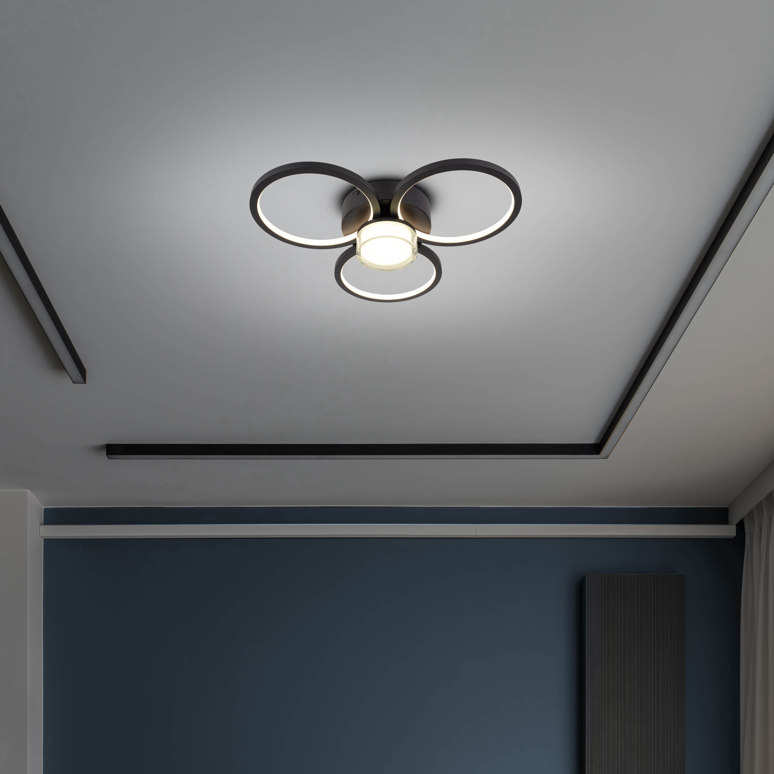 Deckenleuchte mit kreisförmigem Design. Die Decke ist weiß mit dunkelgrauen Akzenten. Die Wände sind blau.