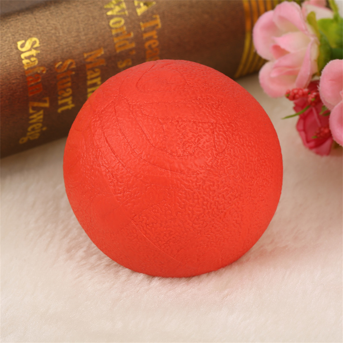 Ein roter Stressball auf einer weißen, flauschigen Oberfläche. Im Hintergrund sind ein Buch und Blumen.