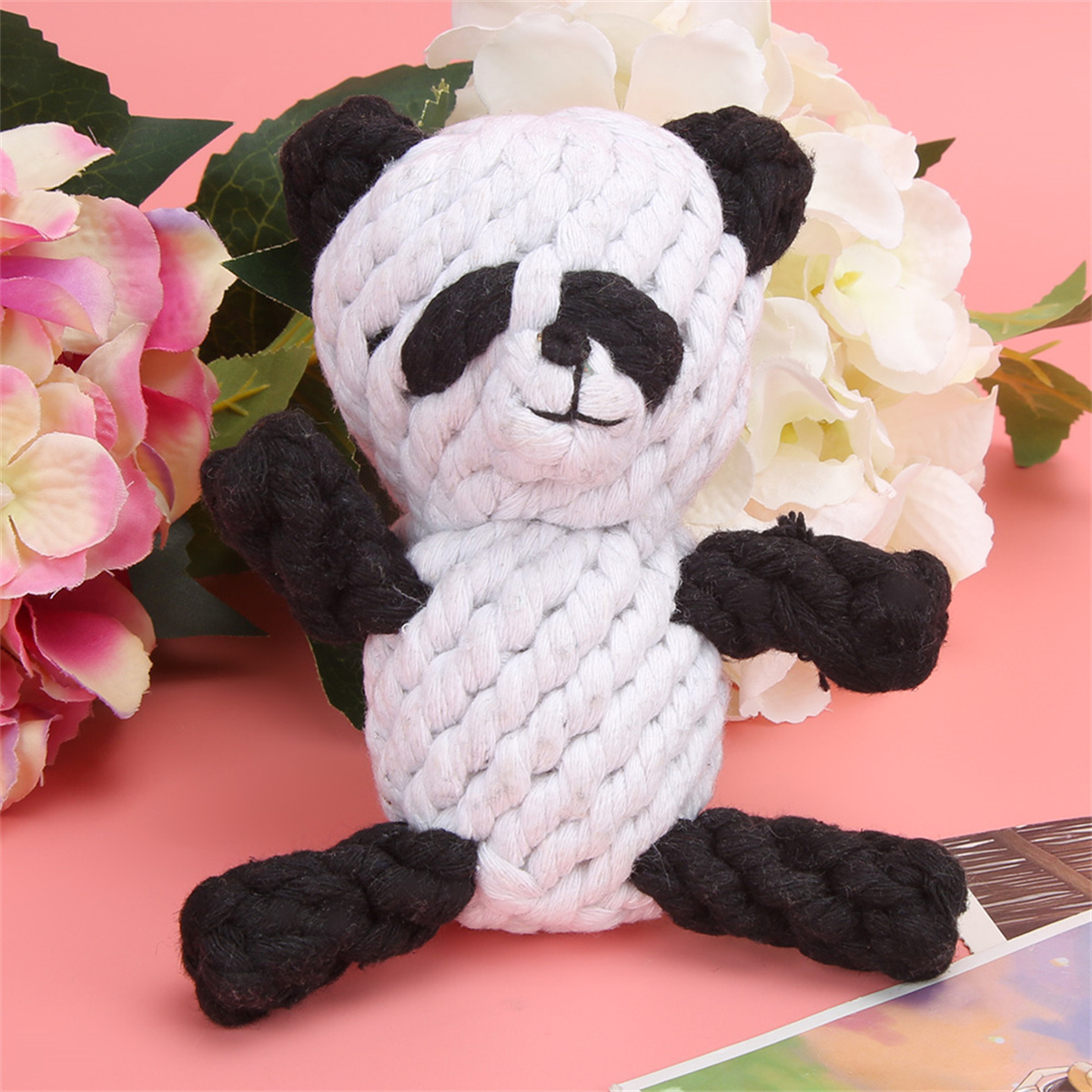 Ein Panda-Stofftier aus weißem und schwarzem Seil auf rosa Oberfläche.