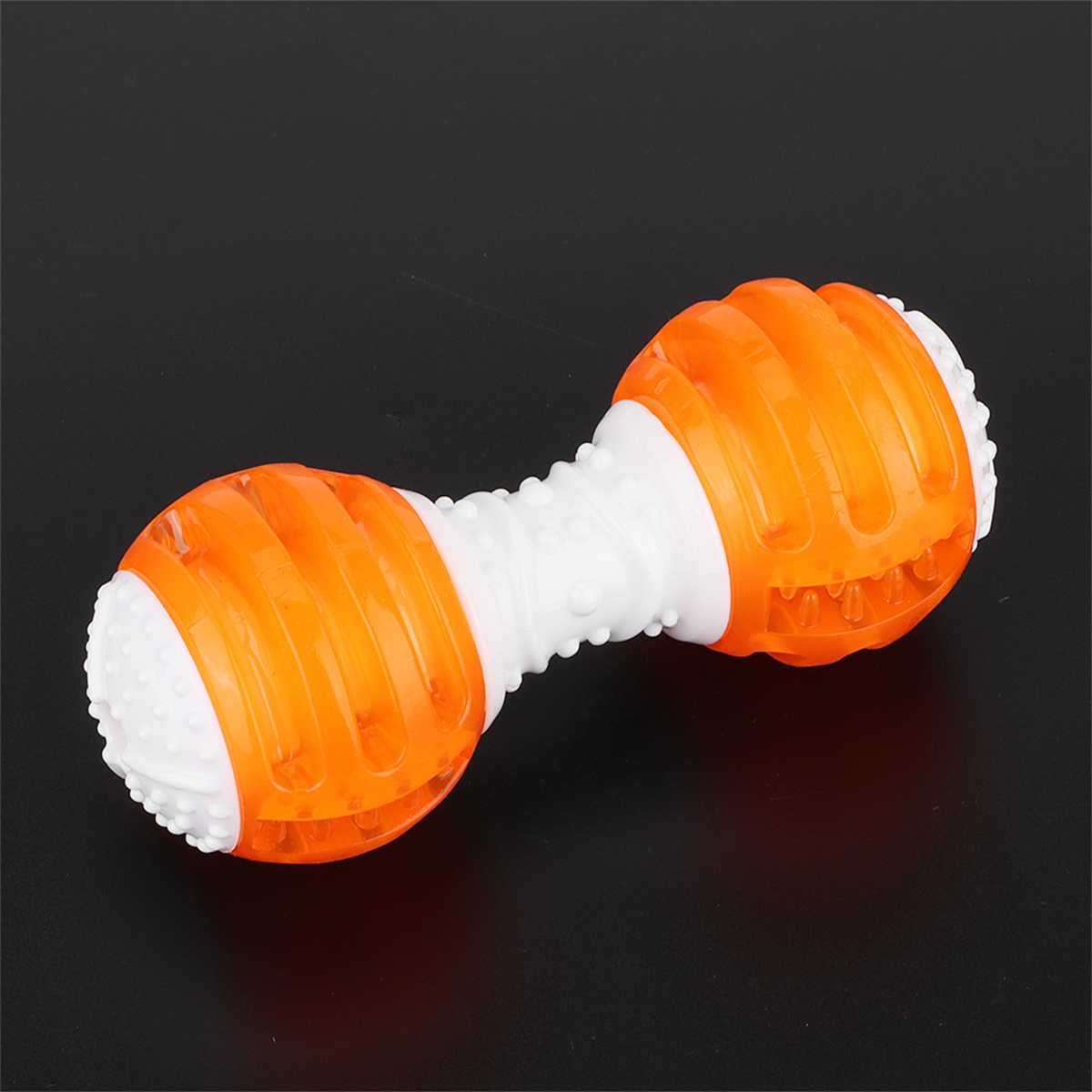 Ein hantelförmiges Hundespielzeug. Es ist orange und weiß. Der Hintergrund ist schwarz. Die Hantel hat Rillen.