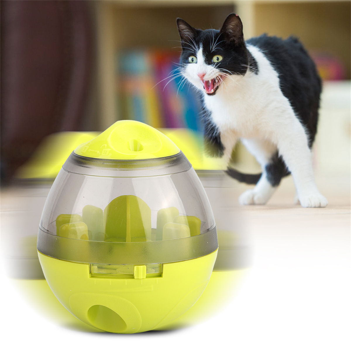 Eine Katze mit offenem Mund betrachtet ein eiförmiges Katzenspielzeug. Das Spielzeug ist grün, klar und hat gelbe Akzente.