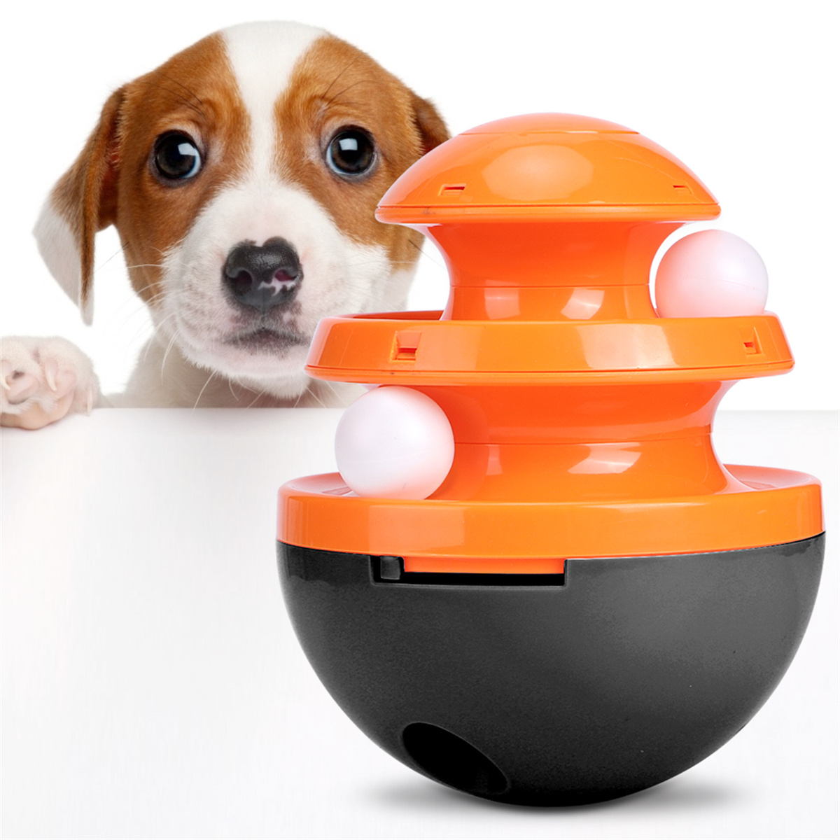 Hundespielzeug mit zwei weißen Kugeln. Oranges und schwarzes Spielzeug, mit einem Welpen, der zuschaut. Weißer Hintergrund.