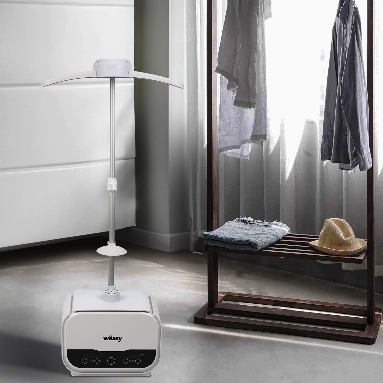 Un vaporizzatore per indumenti bianco con vestiti appesi a un portabiti in legno e un cappello.