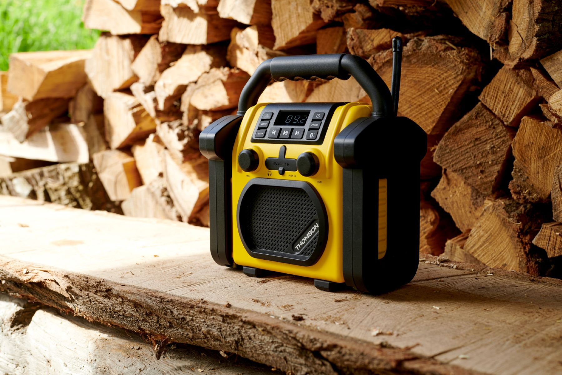 Żółto-czarne radio stojące na drewnianej powierzchni z tłem z pociętych kłód.