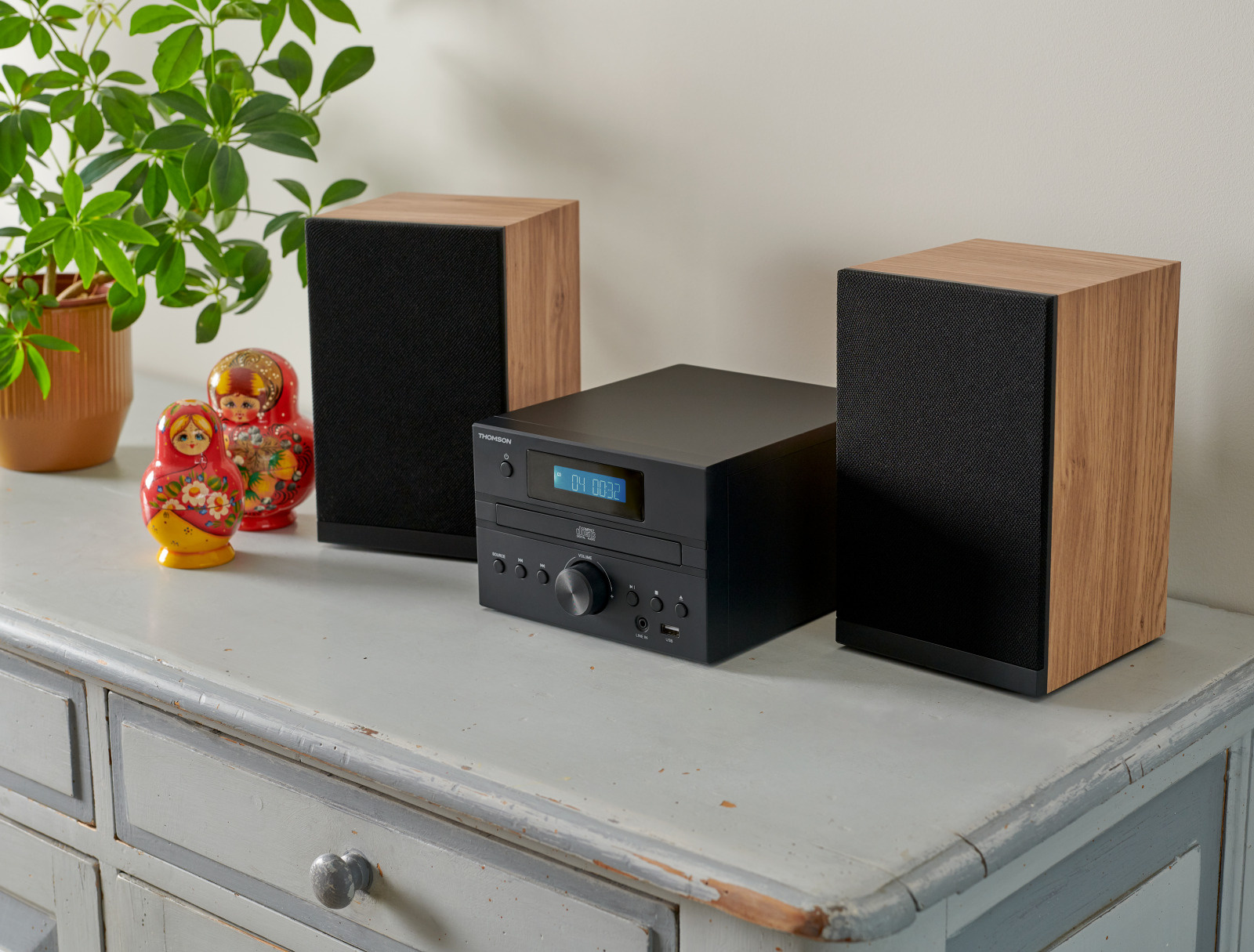 System stereo z głośnikami, czarną jednostką i dekoracyjnymi lalkami na półce.