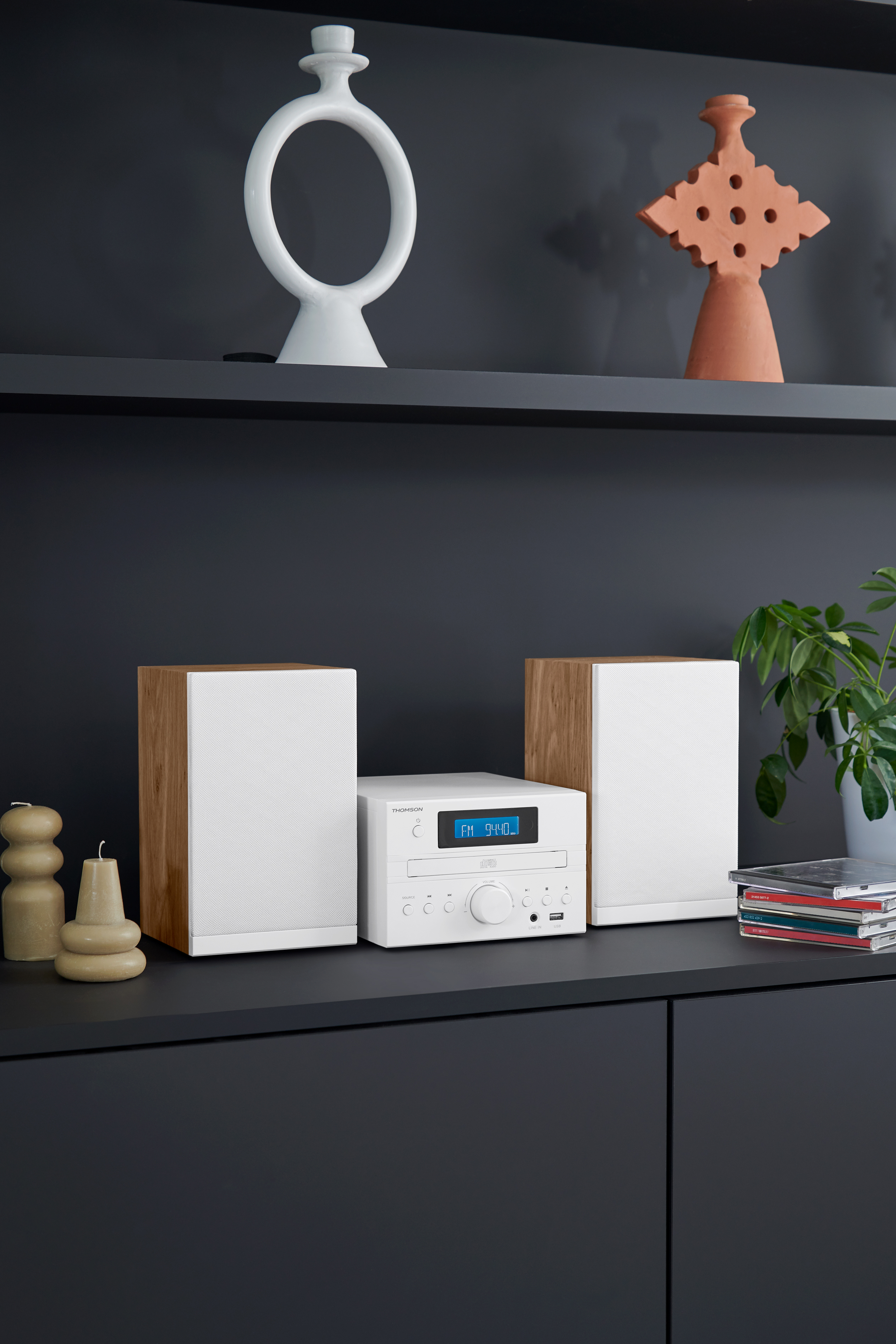 Białe stereo z głośnikami. Stereo ma wyświetlacz. W tle znajdują się półki.