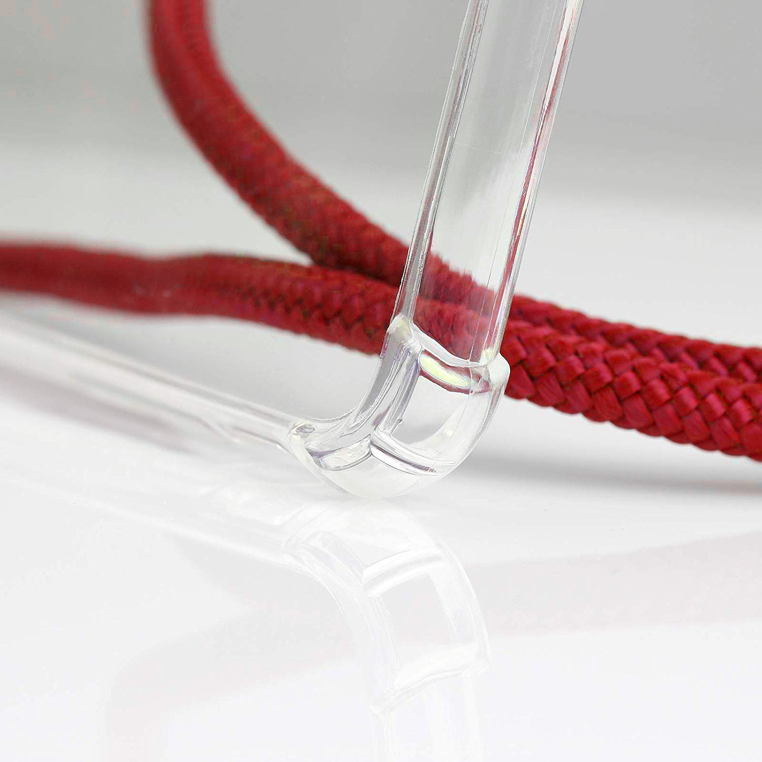 Custodia trasparente per telefono con una corda intrecciata rossa. La custodia è visibile. Sfondo bianco con riflesso.
