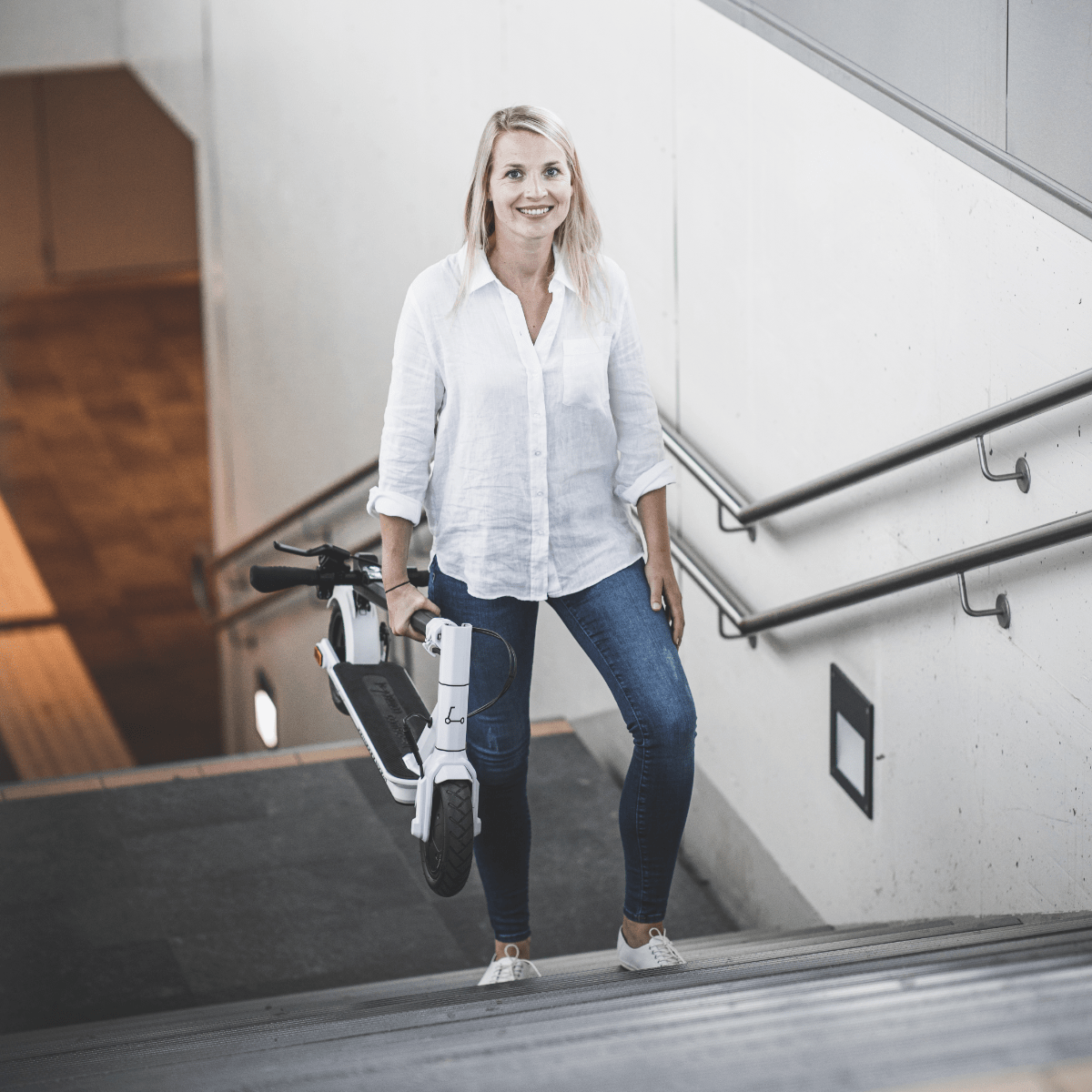 Blonde Frau, die einen weißen Roller hält und Treppen hochgeht.