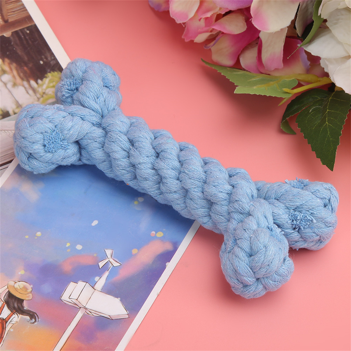Blaues Hundeknochenspielzeug auf rosa Oberfläche mit Blumen. Das Knochen hat eine gedrehte Form.