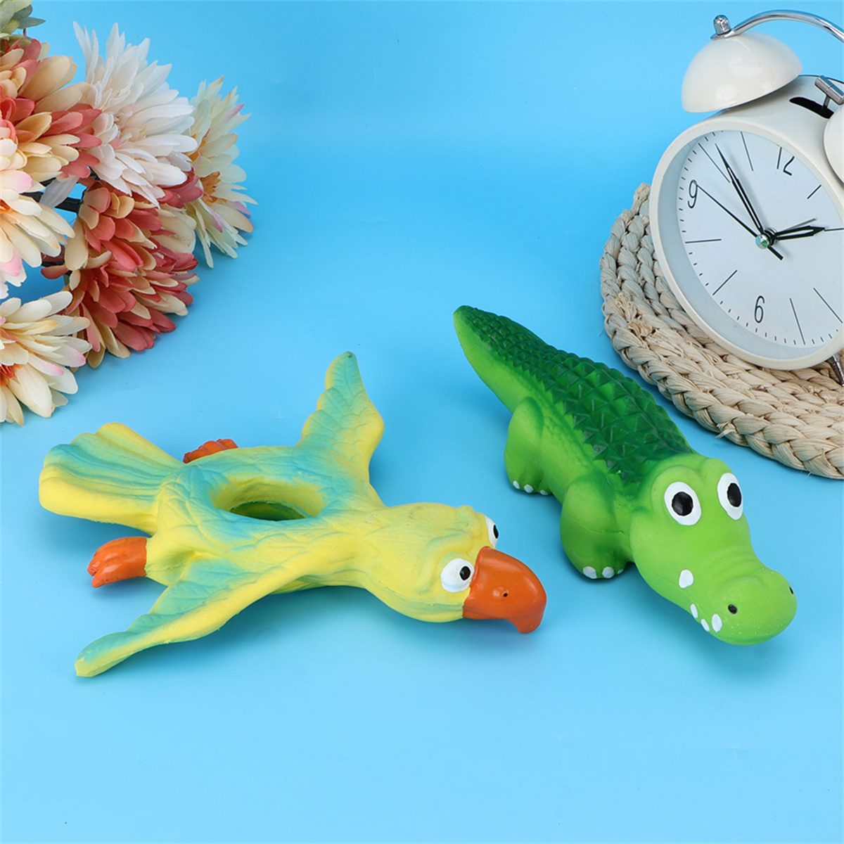 Spielzeugpapagei und Krokodil auf blauem Untergrund, mit Uhr und Blumen im Hintergrund.