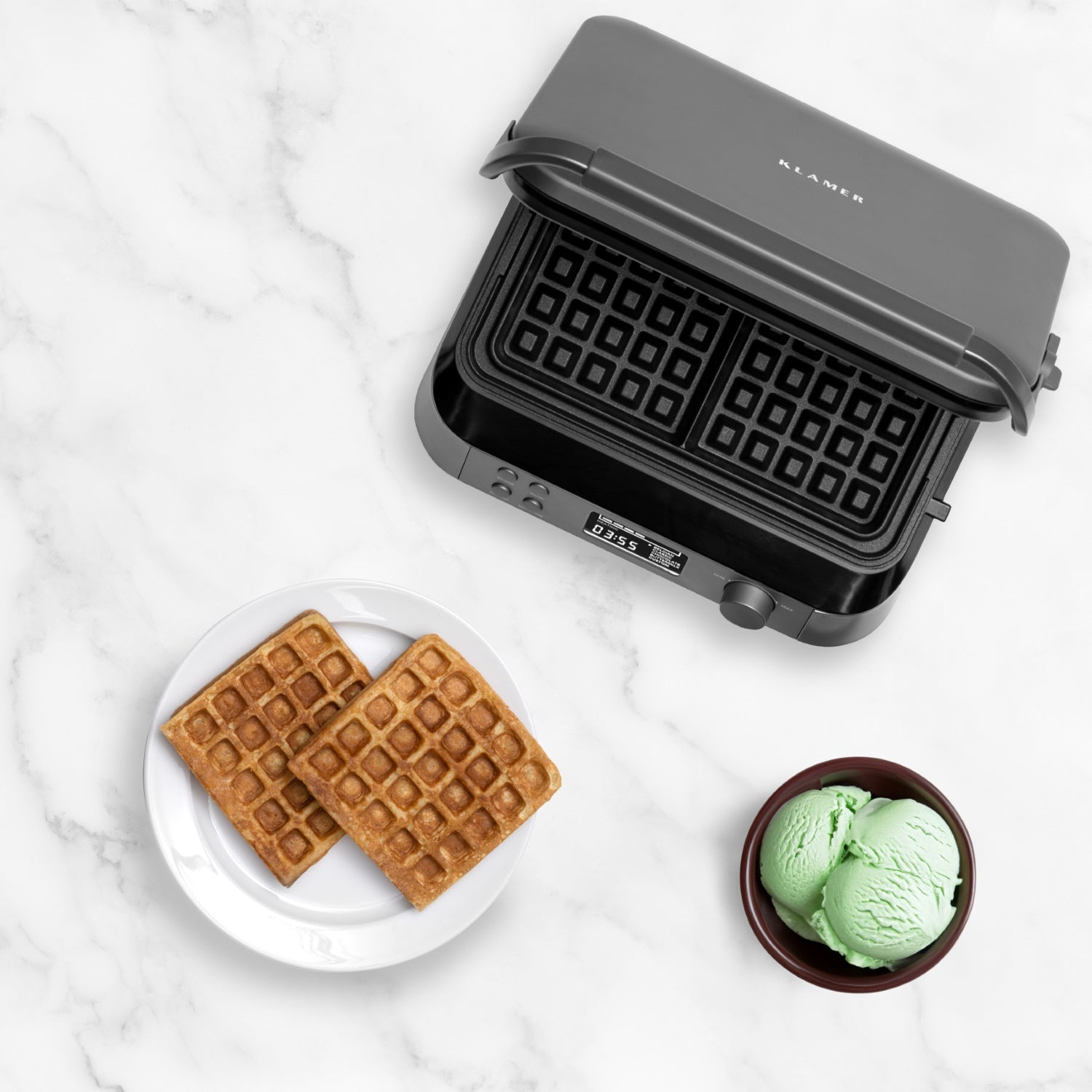 Ein Waffeleisen mit zwei Waffeln auf einem Teller und einer Schüssel mit grünem Eis.