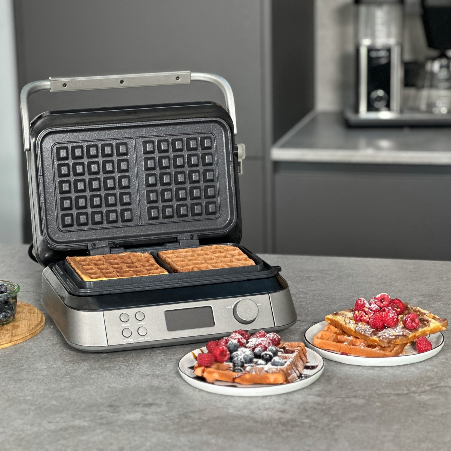 Ein Waffeleisen mit Waffeln. Waffeln sind auf Tellern mit Beeren.