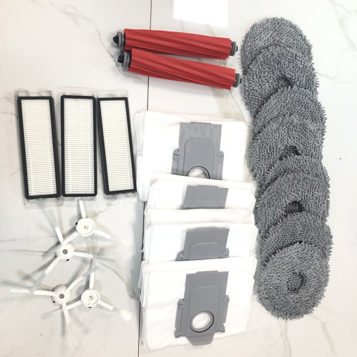 Części robota sprzątającego, w tym szczotki, filtry i nakładki do mopowania, ułożone na białej powierzchni.