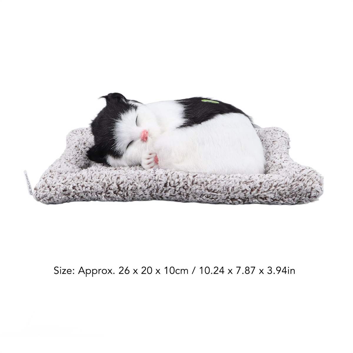 Ein schlafendes Katzenspielzeug auf einem grauen Bett. Die Katze ist schwarz und weiß. Text lautet ca. 26x20x10cm.