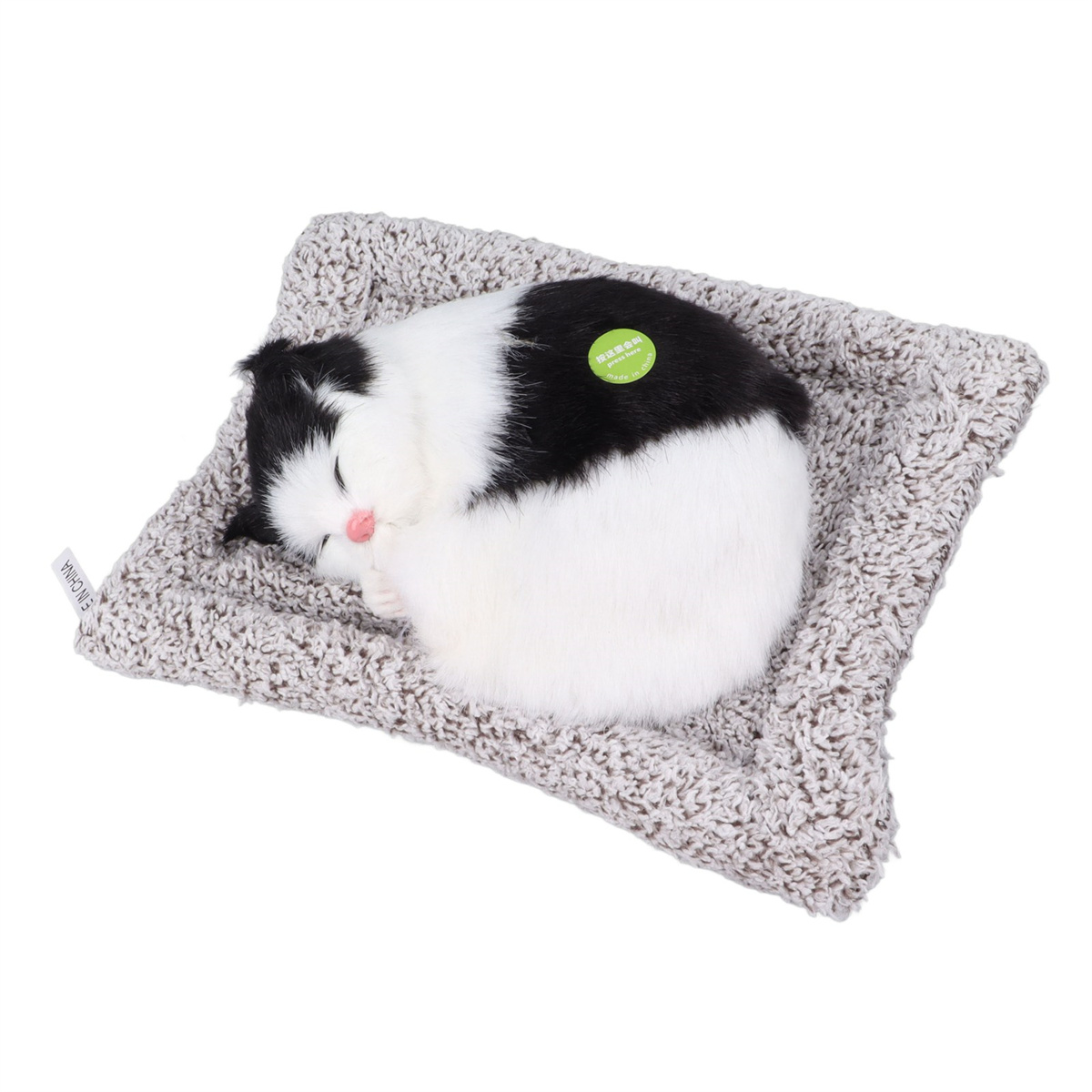 Schlafendes weißes und schwarzes Katzenplüsch auf einem grau gemusterten Bett. Weißer Hintergrund.