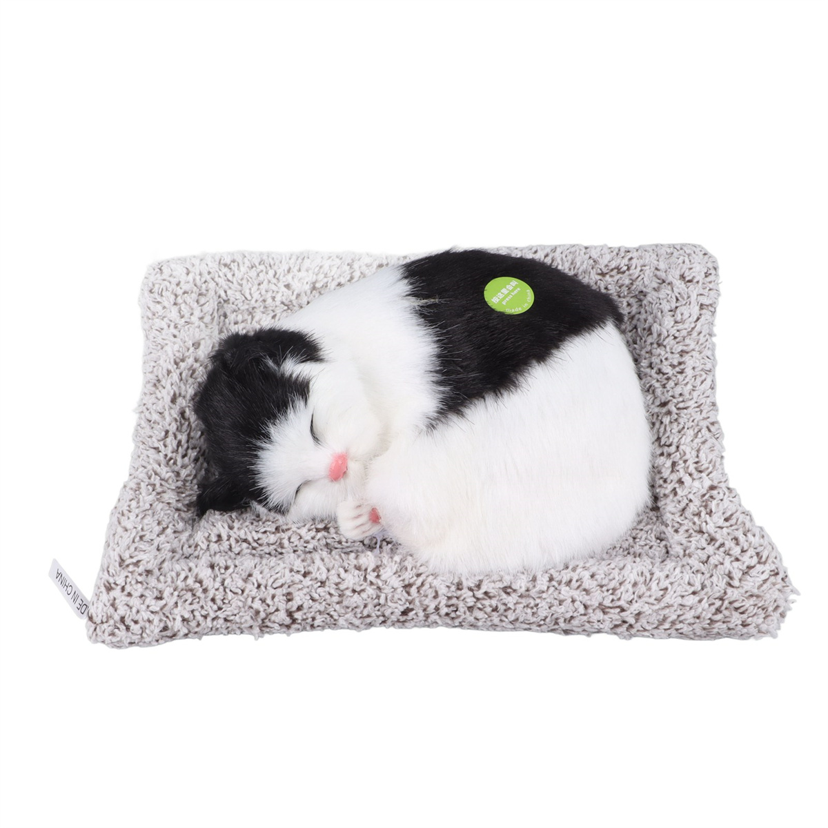 Ein schlafendes schwarz-weißes Katzenplüschtier auf einem grauen Bett. Die Katze ist zusammengerollt, Nase rosa.