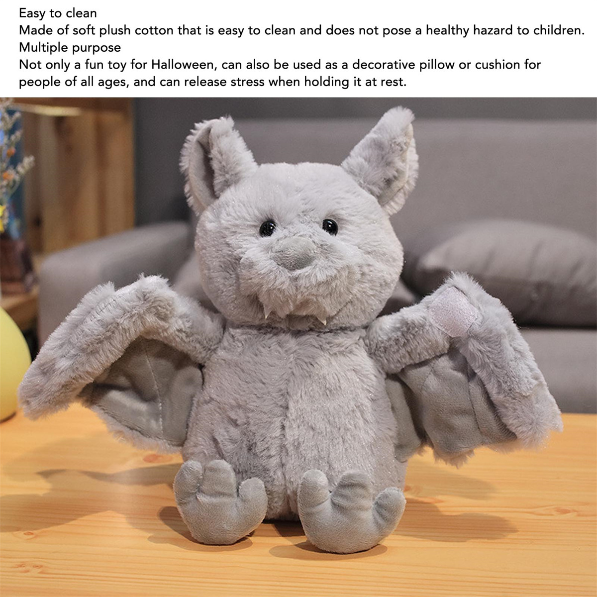 Graue Plüschfledermaus mit offenen Flügeln. Es hat Augen und einen Fleck. Auf einem grauen Sofa.